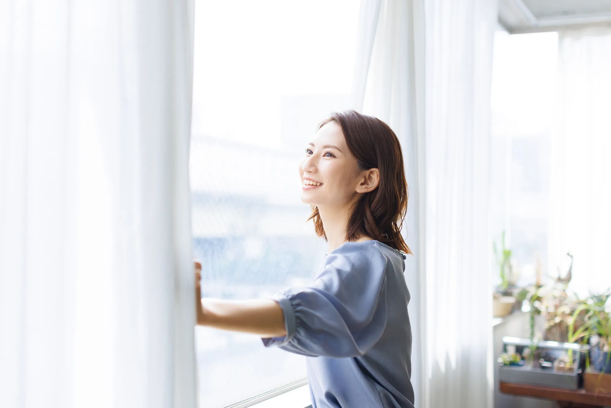 日差しが差し込むリビングのカーテンを開け、外を眺める女性