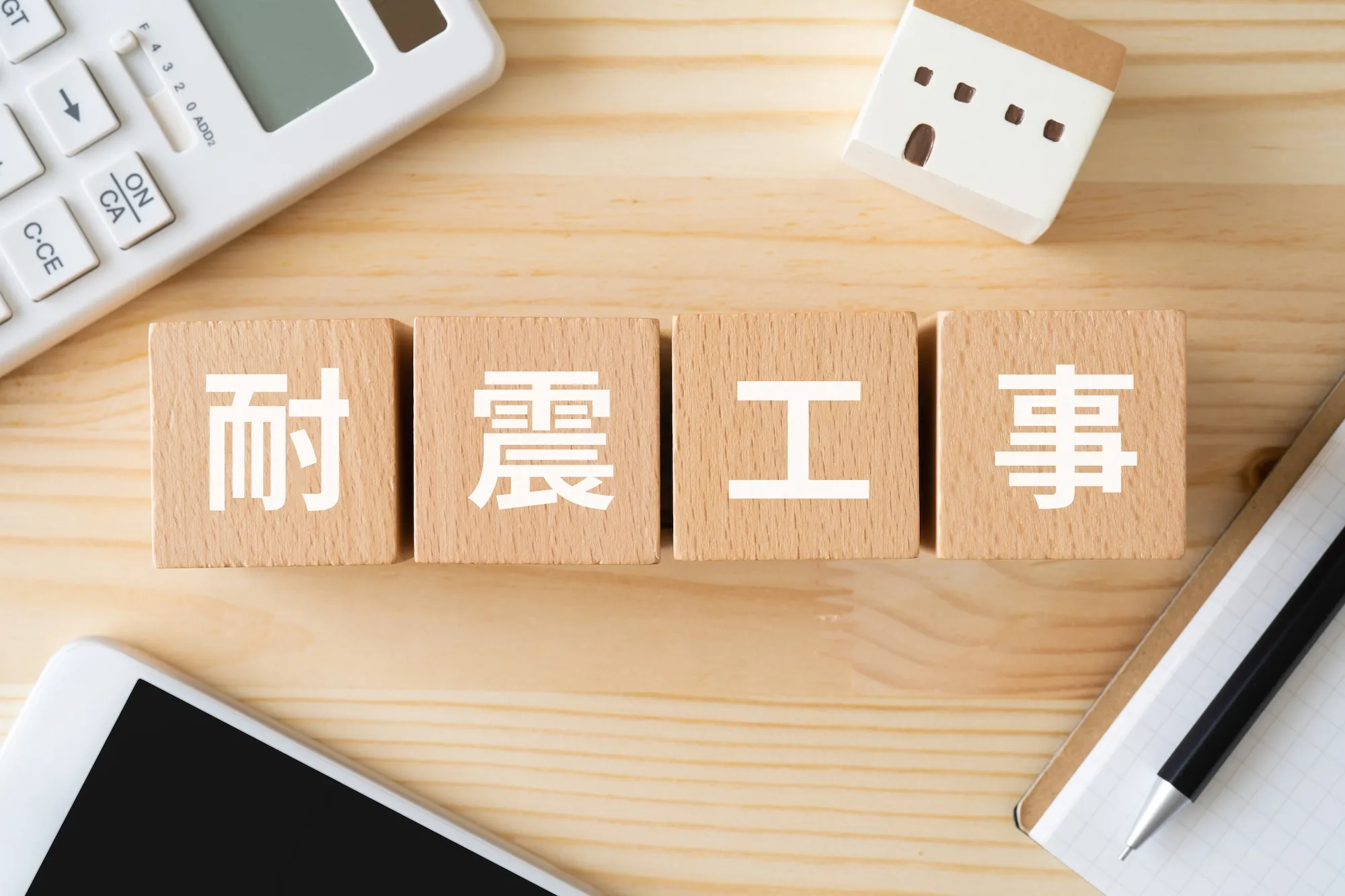耐震工事と書かれたブロック、電卓、スマホ、ミニチュアの家