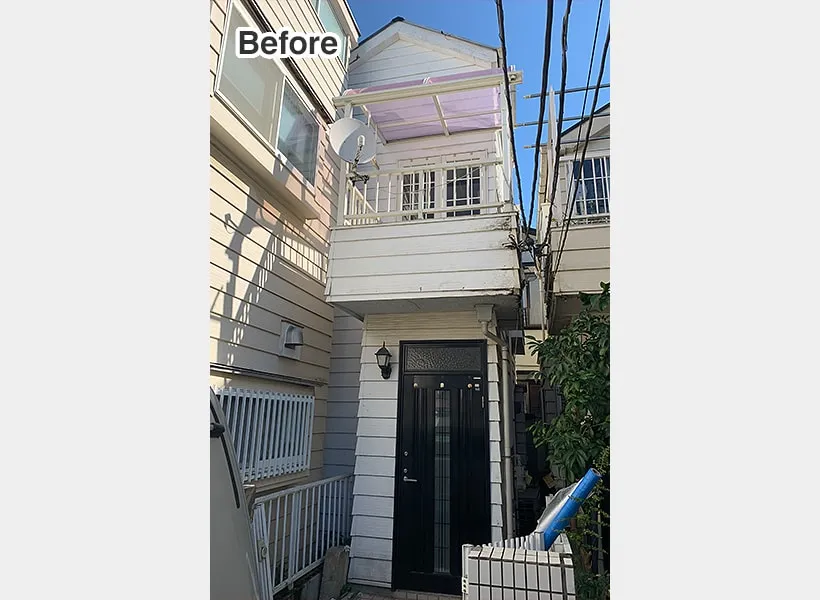 白い外壁や2階バルコニーの老朽化が目立つ住宅の外観