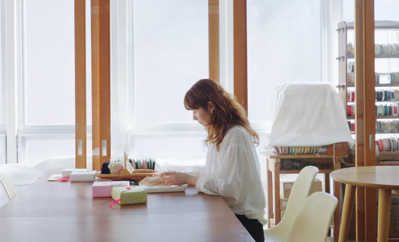 明るい作業部屋で贈り物を丁寧にラッピングしているラッピング講師・ペーパーコーディネーターの宮岡宏会さん
