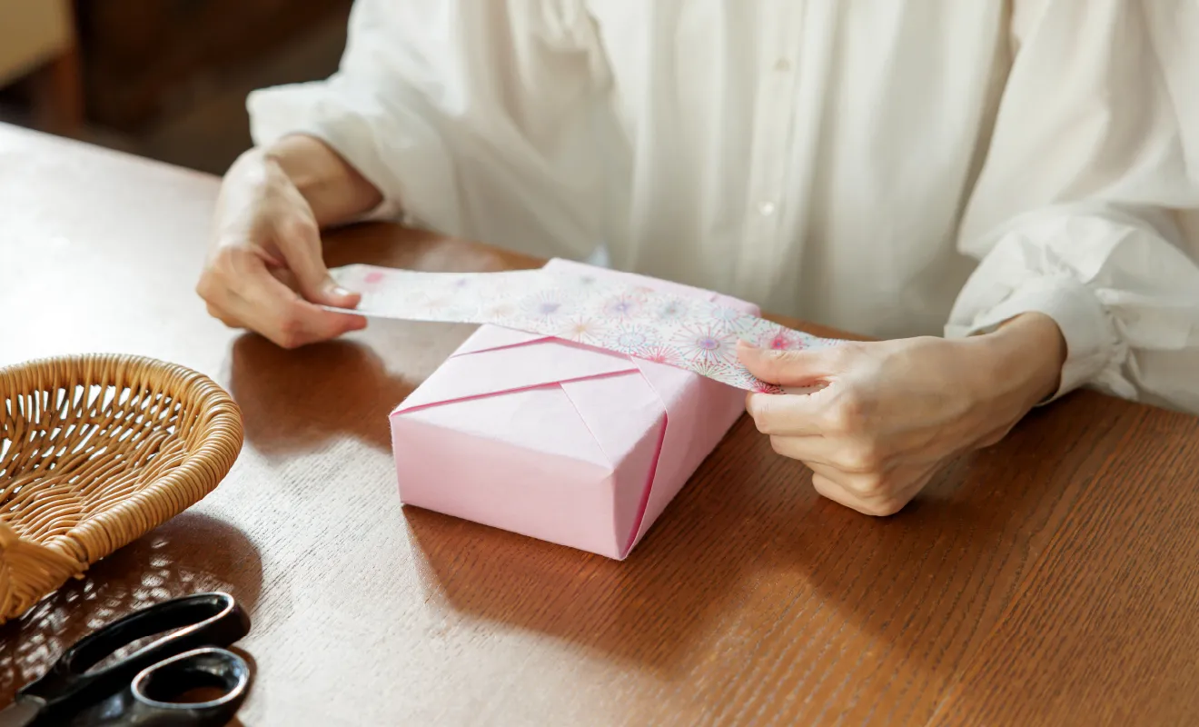 ピンク色のラッピング紙で包んだ箱にリボンを巻くラッピング講師・ペーパーコーディネーターの宮岡宏会さん
