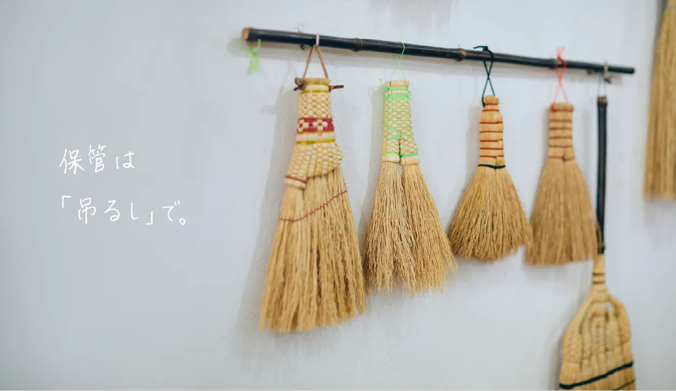 壁の棒に吊るされたミニ箒と『保管は「吊るし」で。』の文字
